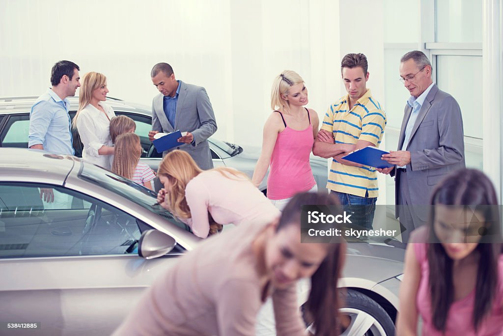 Large group of people at the car exhibition. Large group of people choosing and buying a new car in showroom.    Car Dealership Stock Photo