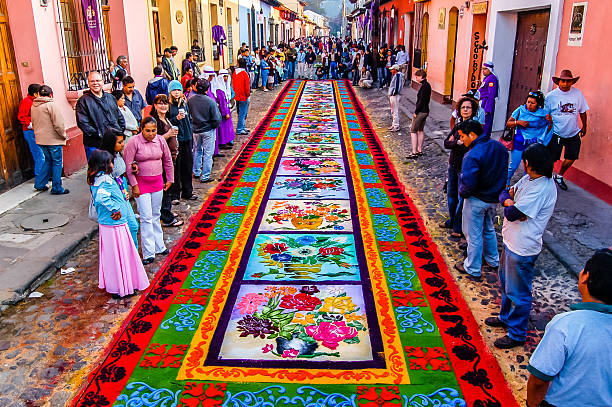 Holy Week carpet, Antigua, Guatemala Antigua, Guatemala - April 10, 2009: Spectators admire Holy Week carpet on Good Friday morning in Spanish colonial town & UNESCO World Heritage Site with most famous Holy Week celebrations in Latin America. Groups work all night to make carpet (using wooden stencils and dyed sawdust) in path of Good Friday procession. Purple clad 'cucuruchos' take turns to carry religious floats in processions. guatemala stock pictures, royalty-free photos & images