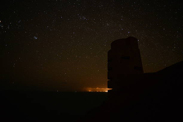 Les Landes, Jersey, U.K. Wide angle astrophotography image using a long exposure and high ISO, of an uninhabited WW2 German bunker/tower with light from Guernsey in the background another Channel Island. world war galaxy stock pictures, royalty-free photos & images