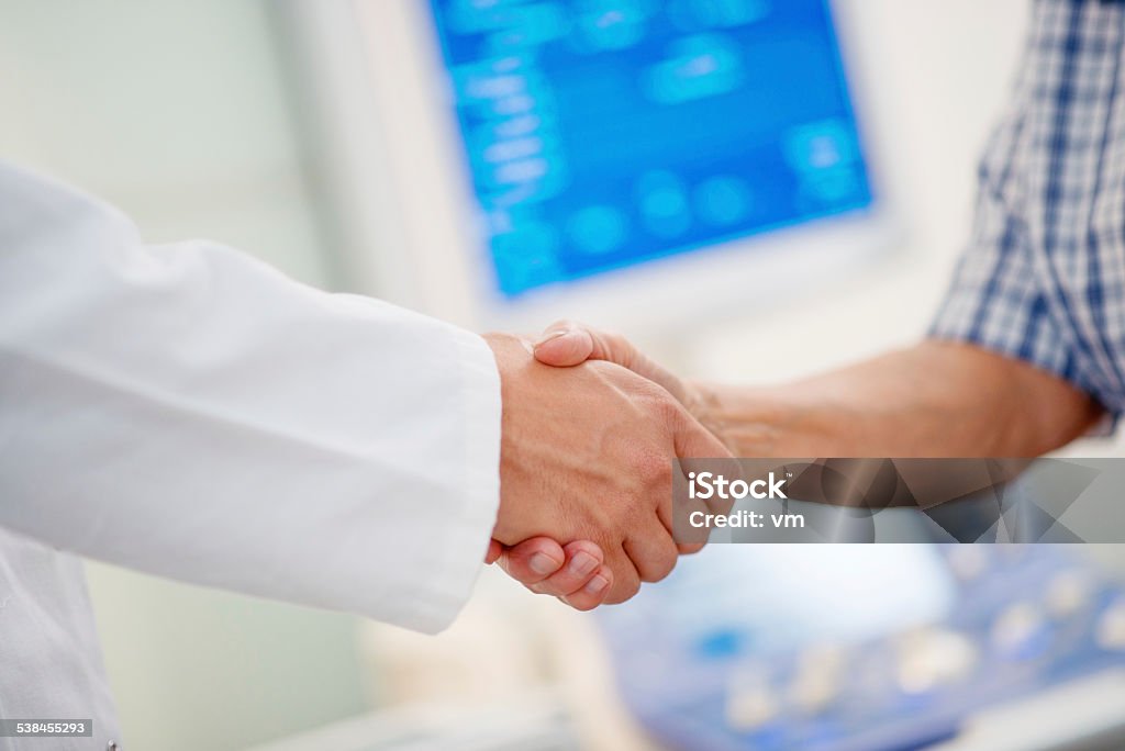 Doctor and Patient Shaking Hands Firmly Close up of doctor shakes hands with a patient in laboratory. Defocused Stock Photo