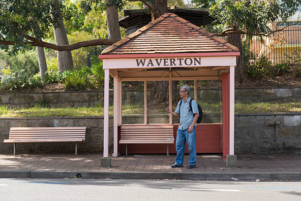 Mature Asian man reading text messages on a mobile phone while waiting for public buses at the bus stop, Suburb Sydney Australia.