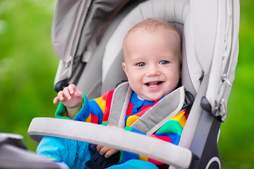 Baby boy in warm colorful knitted jacket sitting in modern stroller on a walk in a park. Child in buggy. Little kid in a pushchair. Traveling with young kids. Transportation for family with infant.