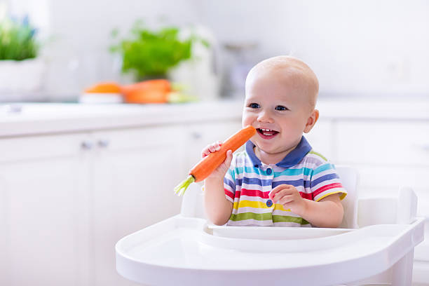 маленький милый ребенок ест морковь - baby carrot snack healthy eating small стоковые фото и изображения