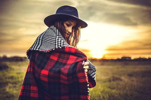Girl with big hat enjoying in sunset wrapped in red plaid blanket