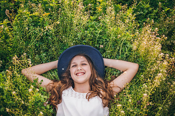 Child girl in straw hat dress in wheat spikelets field. Smiling kid in sunglasses on sunset countryside landscape. Family farming agriculture environment ecology concept. Cottagecore style aesthetic.