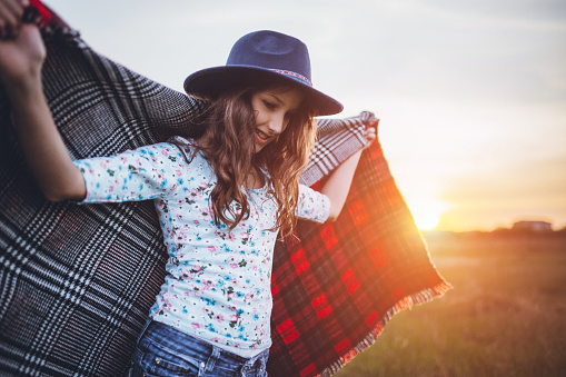 Girl with big hat enjoying in sunset wrapped in red plaid blanket