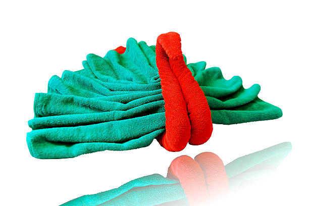 This is a close up photo of a cobalt blue, terry cloth towel, folded to depict a rose bloom.  The flower is centered in the photo, turned at a very slight angle to the right.  The background is stark white.  The edges of the towel appear to blur against the white background. 