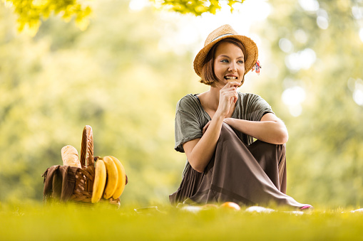 Young woman relaxing in nature at picnic and eating a sweet snack.
