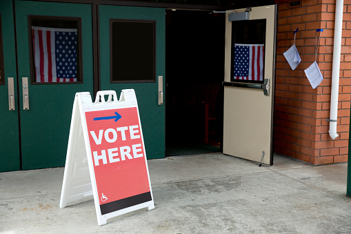 Stock photo of a vote here sign at an American voting location with American flags in the background