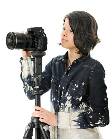 An attractive young teen patiently waiting for the right moment before clicking her tripod held camera for a great shot.   On a white background.