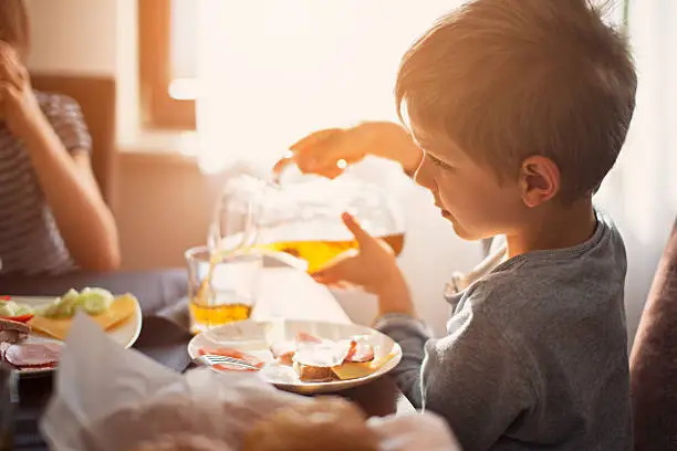 Kids eating breakfast. Little boy is pouring apple juice to a glass. The boy is aged 6 and the girl is aged 10.