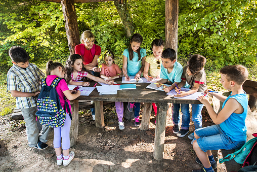 Large group of children drawing with their teacher on a filed trip in the park.