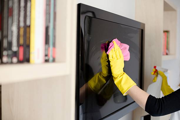 Woman in yellow rubber gloves cleaning tv stock photo