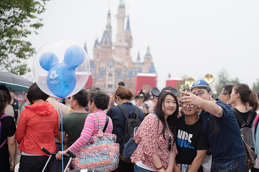 Shanghai, China - June 7, 2016: A group of young chinese people taking a selfie with the Enchanted Castle on the back,  during trial operations before the grand opening of Shanghai Disneyland Park, located in Chuansha New Town of Pudong New Area, which is officially confirmed to open on June 16th, 2016. Is the sixth in the world and the second in China (after Hong Kong Disneyland).