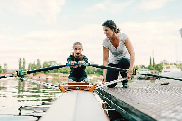 Single scull rowing. 12 years girl rowing single scull. She is preparing for new competitions. Rowing on Sava river. Coach giving instructions to girl rowing. Her mother is her coach.