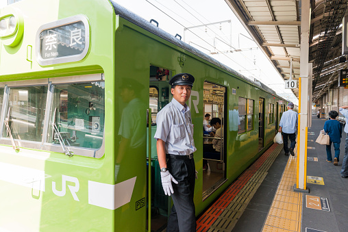 Kyoto, Japan - May 31, 2016: At Kyoto Station a JR Train conductor stands on the platform waiting for the train  to depart as passengers walk in the background.