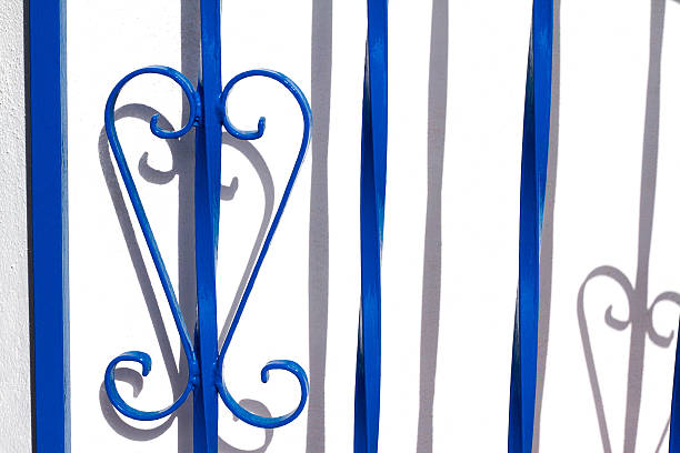 Sicily style: Close-up shot of an ornate blue wrought-iron gate detail against a bright white wall. Shot in the Aeolian Islands, Sicily, Italy.
