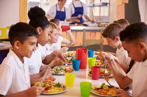 um escola primária de crianças comer em uma mesa de escola cantina - child food school children eating imagens e fotografias de stock