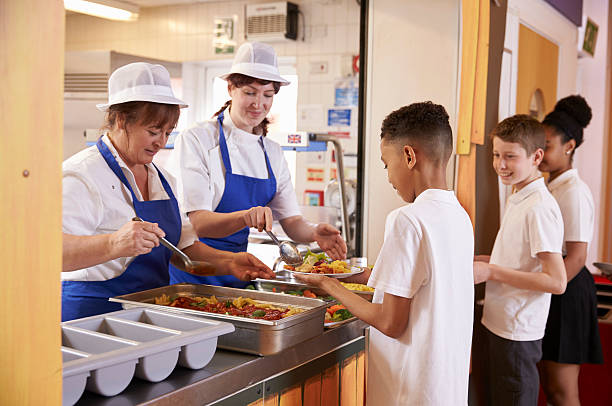 two women serving food to a boy in a school cafeteria - schoollunch stockfoto's en -beelden