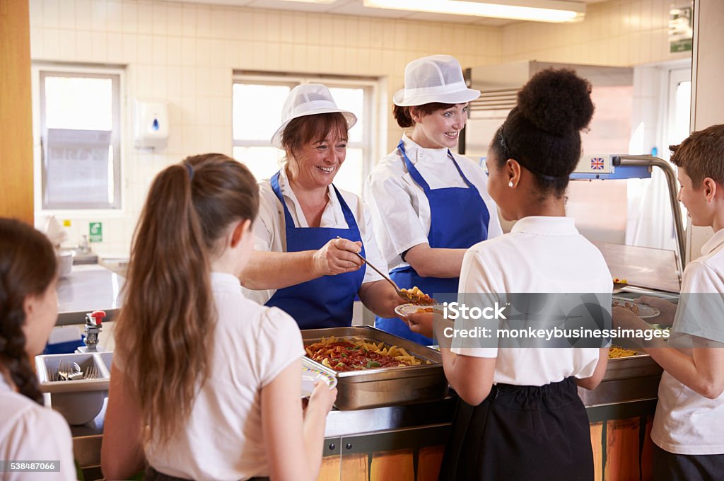 Two women serving kids food in a school cafeteria, Two women serving kids food in a school cafeteria, back view School Building Stock Photo
