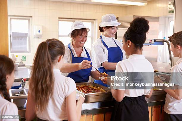Two Women Serving Kids Food In A School Cafeteria Stock Photo - Download Image Now - School Building, Education, Meal