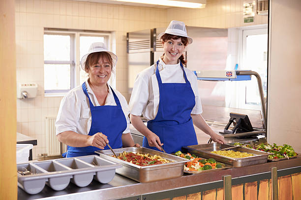 Two women waiting to serve lunch in a school cafeteria Two women waiting to serve lunch in a school cafeteria cafeteria worker photos stock pictures, royalty-free photos & images