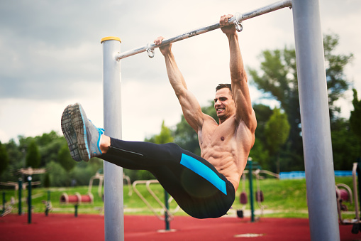 Young muscular build man is making an effort while exercising on exercise equipment at outdoor gym.