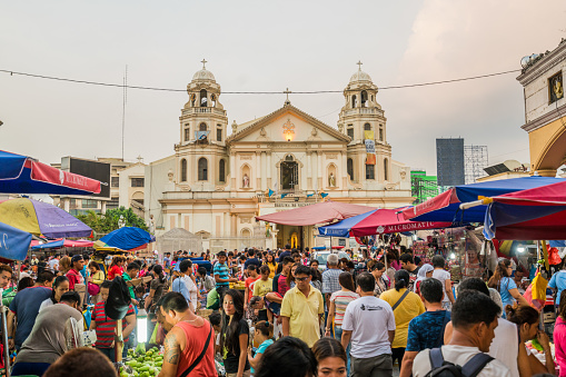 Manila, Philippines - May 17, 2016: View of the Quiapo Church and the crowded plaza during twilight. People are seen walking around and browsing through several street shops set up in front of the church.