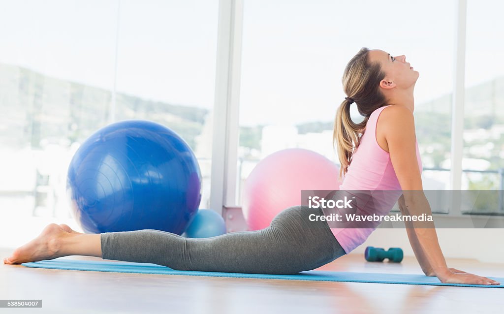 Fit woman doing the cobra pose in fitness studio Side view of a fit young woman doing the cobra pose in a bright fitness studio 20-29 Years Stock Photo