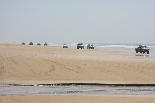 A line of four wheel drives cruise along the beach on Fraser Island, Queensland, Australia.