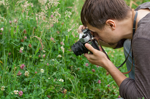 Man is photographing flowers in green grass by means of vintage camera.