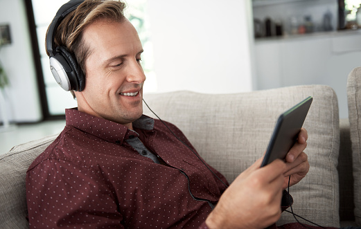 Shot of a man using headphones and a digital tablet on a sofa at home