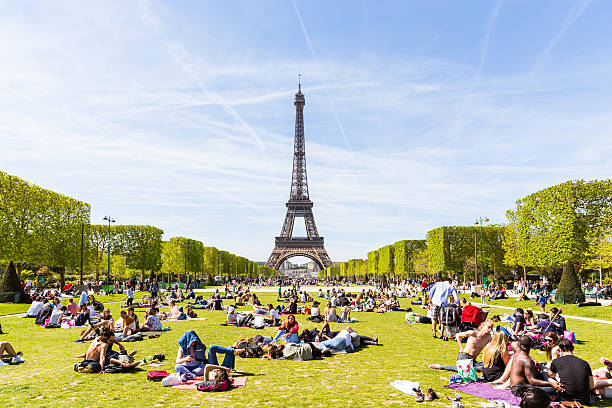 People on Champ de Mars with Eiffel Tower on background Paris, France - May 5, 2016: Lots of people relaxing and having fun on Champ de Mars with the Eiffel Tower on background on a sunny day. champ de mars stock pictures, royalty-free photos & images