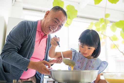 Grandfather smiling and helping his granddaughter to make breakfast in the kitchen. Kyoto, Japan. May 2016