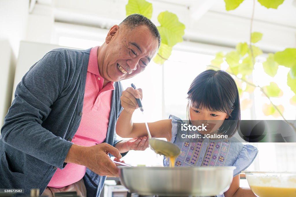 Grandfather teaching his granddaughter to cook Grandfather smiling and helping his granddaughter to make breakfast in the kitchen. Kyoto, Japan. May 2016 Grandparent Stock Photo