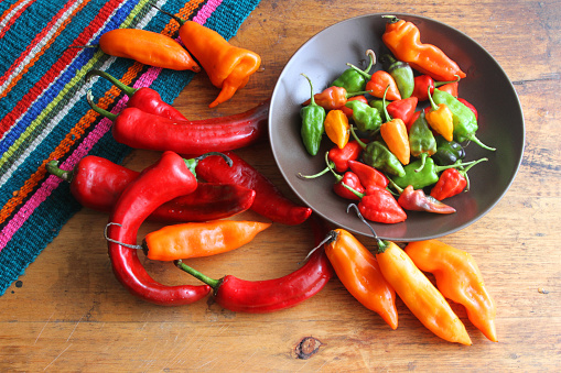 Overhead view of group of colorful chili peppers on a rustic table with colorful mat