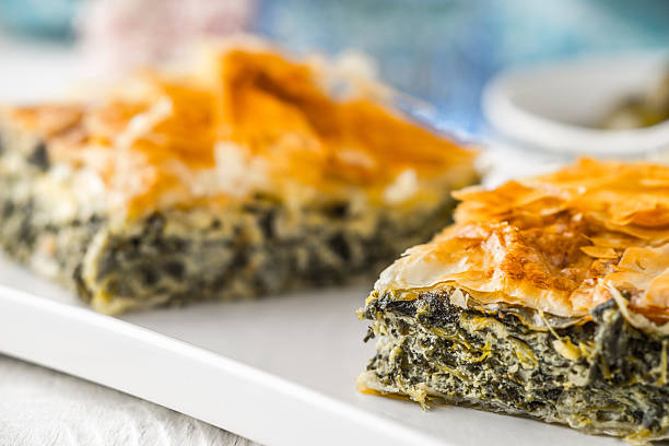 grecki pie spanakopita na białej płycie z rozmytymi akcesoriami poziomymi - tart zdjęcia i obrazy z banku zdjęć