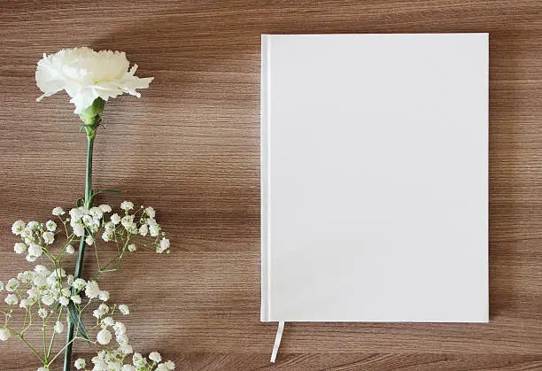 Blank white book, journal, wedding guestbook, notebook mockup. Object for design and branding. White flowers and wooden texture, top view.