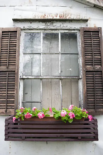 An old unkept window with a beautiful flowerbox.