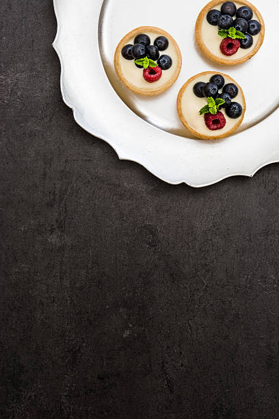 Delicious tartlets with raspberries and blueberries on slate background