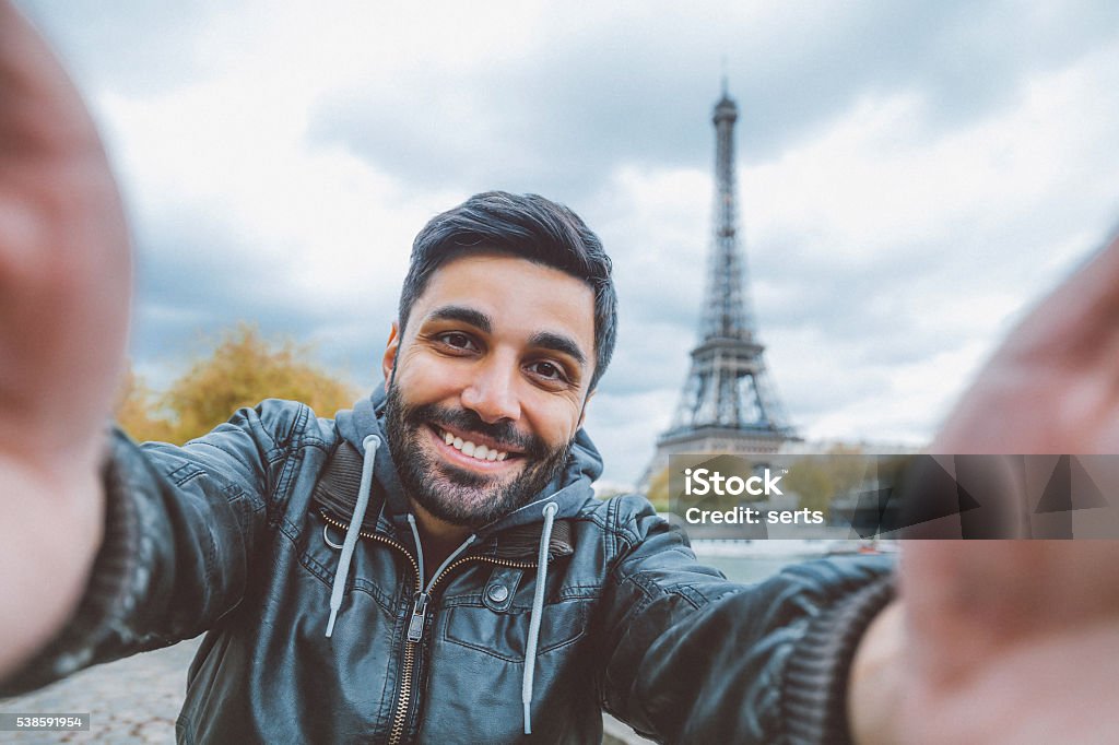 Young man taking selfie with smartphone Young middle eastern man holding smart phone and taking selfie pictures. He is happy, smiling enjoying and looking at her camera at coastline of Seine river against Tour Eiffel in Paris, France.  Selfie Stock Photo