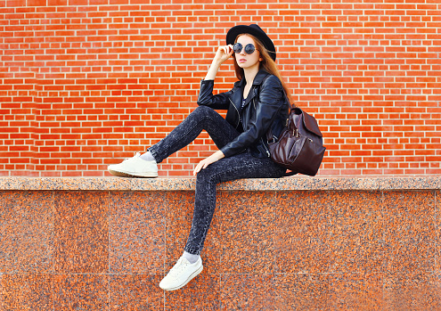 Fashion pretty woman in black rock style sitting in city over bricks background