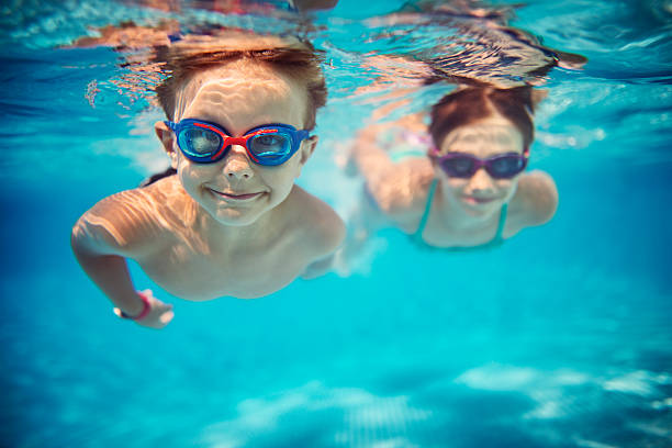 Happy kids swimming underwater in pool Smiling kids enjoying underwater swim in the pool towards the camera. Sunny summer day. Brother aged 5 is in the front, the sister is aged 9 and is swimming in the background. Slightly soft. underwater photos stock pictures, royalty-free photos & images