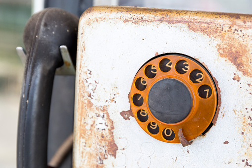 Rusty old vintage rotary pay phone for public use. Old pay telephone with coin slots on a wall.