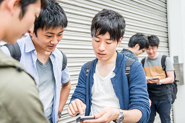 Five male japanese students, friends talking, having fun on the street, Kyoto, Japan, Asia. three are looking at the smart phone, two are chating in the background. Copy space. Nikon D800, full frame, XXXL. iStockalypse Kyoto 2016.