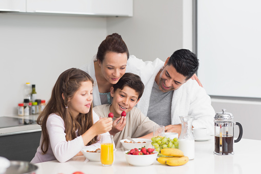 Portrait of happy young kids enjoying breakfast with parents in the kitchen