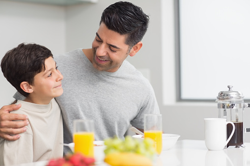 Smiling young son with father having breakfast in the kitchen