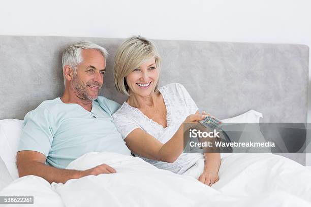 Happy Couple Watching Tv In Bed Stock Photo - Download Image Now - Bed - Furniture, Mature Couple, Sitting