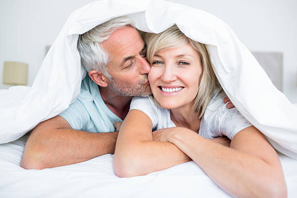 Closeup of mature man kissing womans cheek in bed Closeup of a mature man kissing womans cheek in bed at the home beds stock pictures, royalty-free photos & images