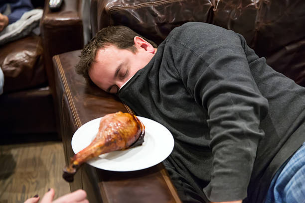 Caucasian man takes nap in a comfortable leather chair A Caucasian man takes a nap in a comfortable leather chair after eating too much for Thanksgiving dinner.  A turkey leg sits on a plate on the armrest.  Shot with Canon 5D Mark 3.  rm funny thanksgiving stock pictures, royalty-free photos & images